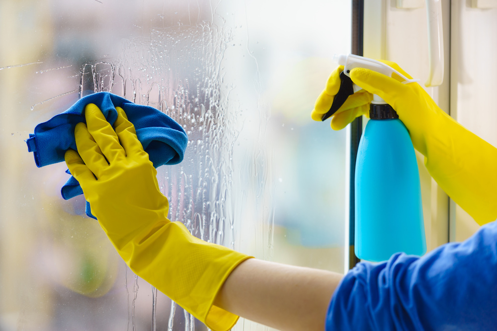 gloved hand cleaning window rag and spray